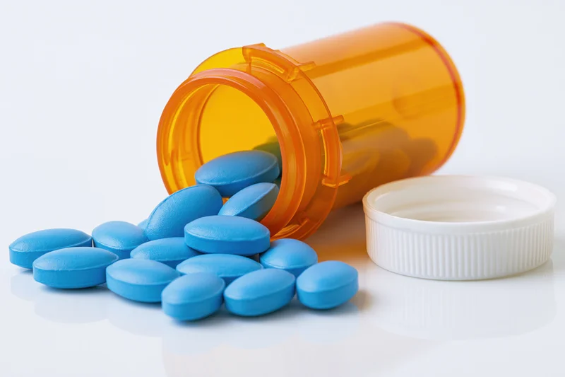 Blue pills spilling from an orange prescription bottle on a white surface