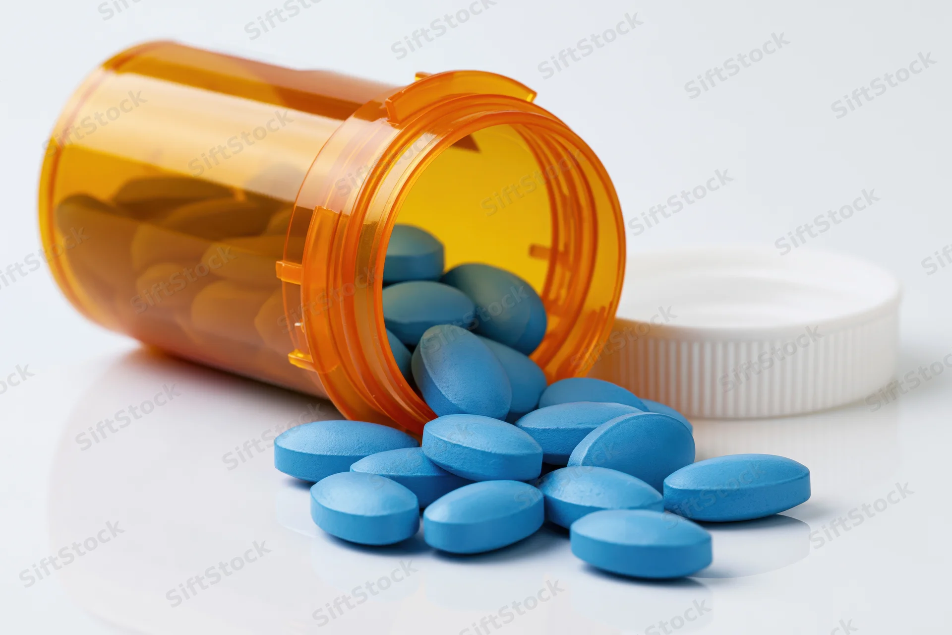 Blue pills spilling from an orange prescription bottle on white surface