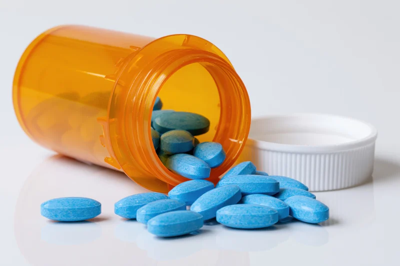 Blue pills spilling from an orange prescription bottle on a white surface