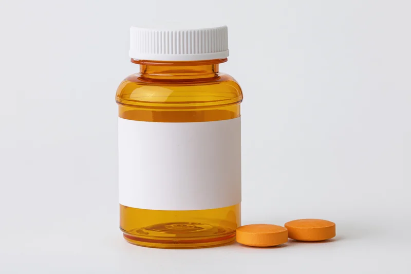 Orange translucent pill bottle with white cap and blank label, two orange tablets beside it on white surface