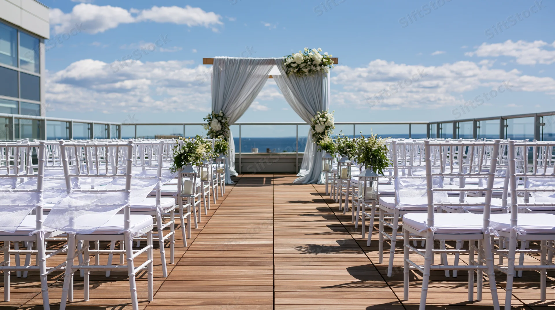 White chiavari chairs arranged on wooden rooftop deck facing floral arch with ocean view