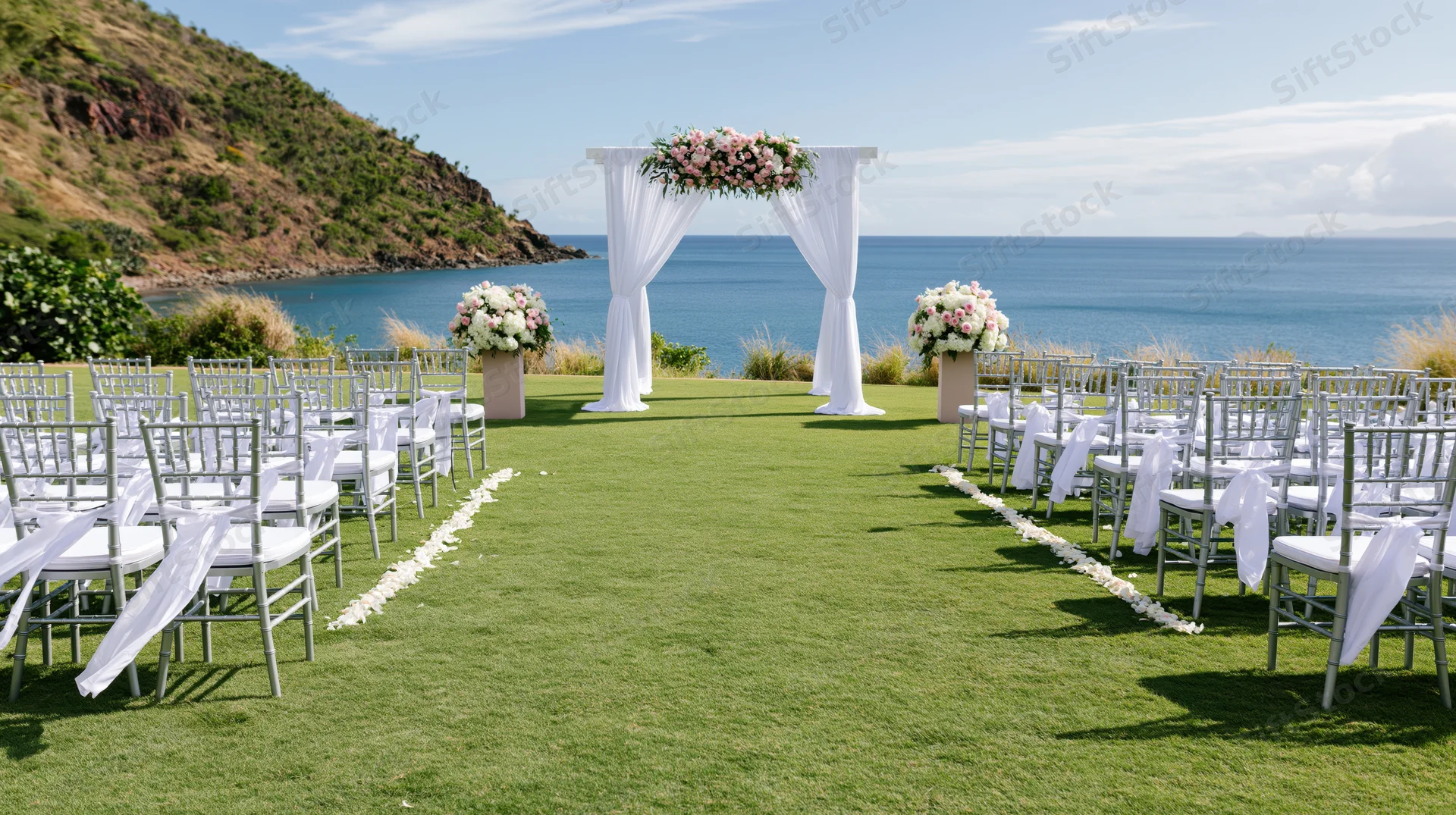 Wedding ceremony setup on manicured lawn overlooking ocean with white chairs and floral arch
