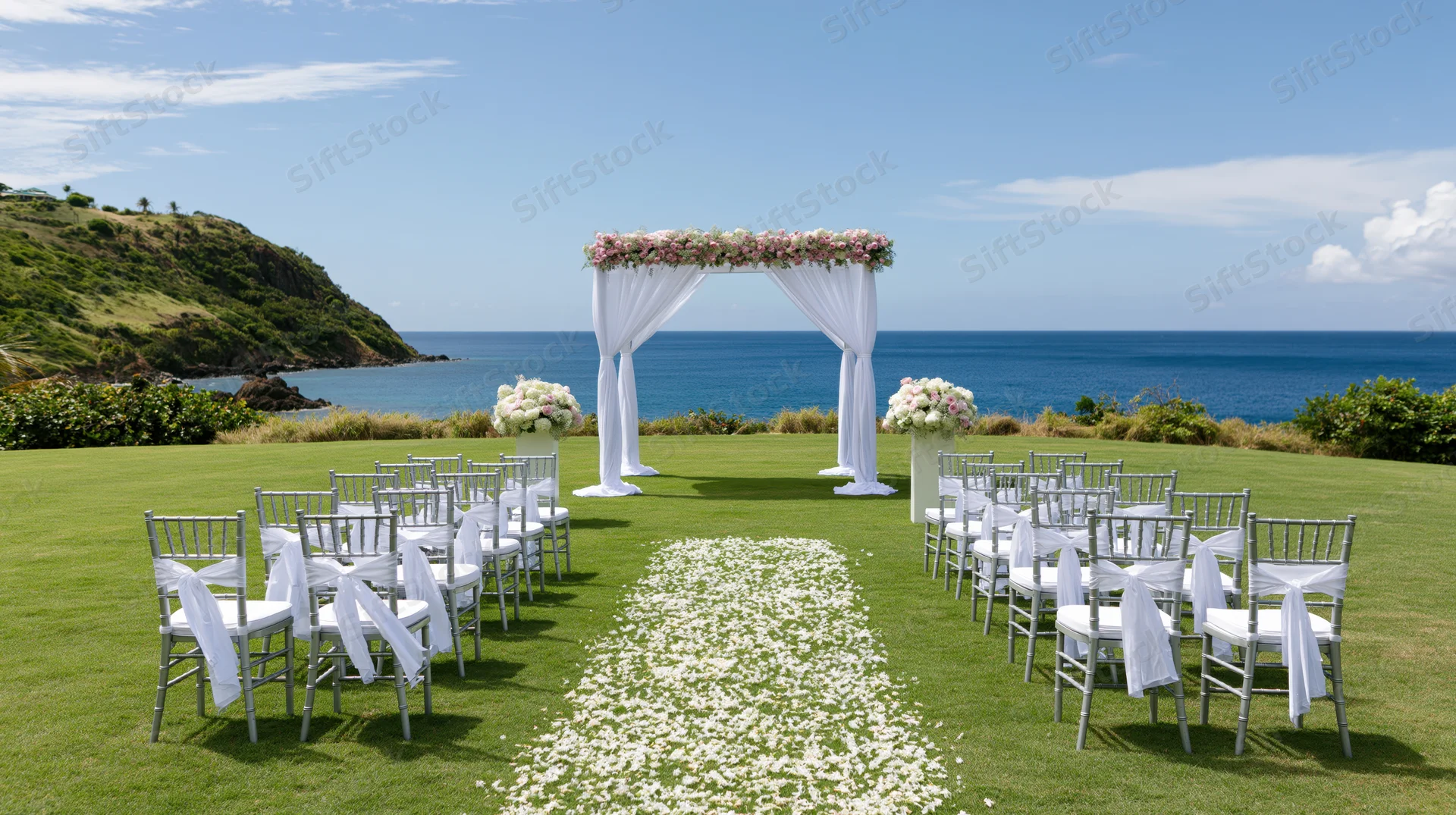 Wedding ceremony setup on manicured lawn overlooking ocean with floral arch and white petals aisle