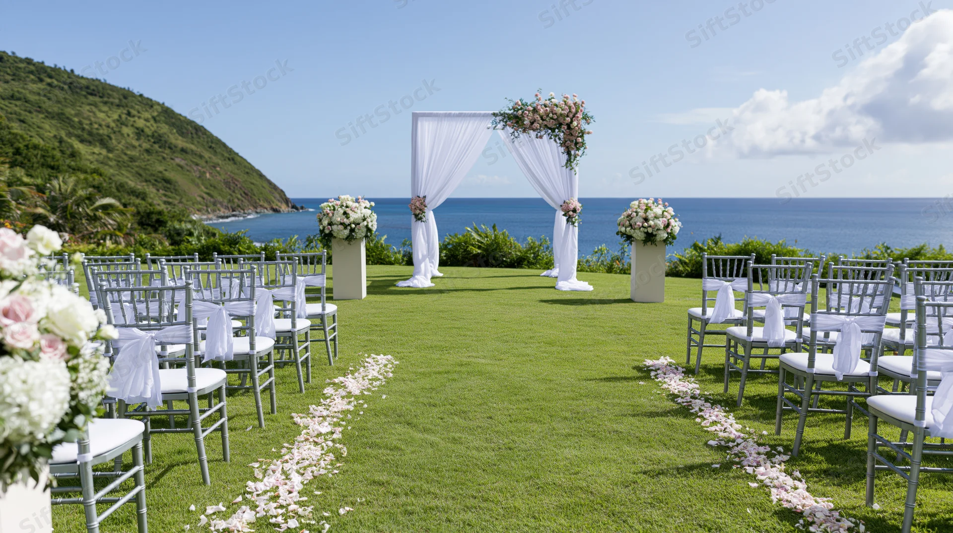 Wedding ceremony setup on a manicured lawn overlooking the ocean with floral arch and aisle lined with petals