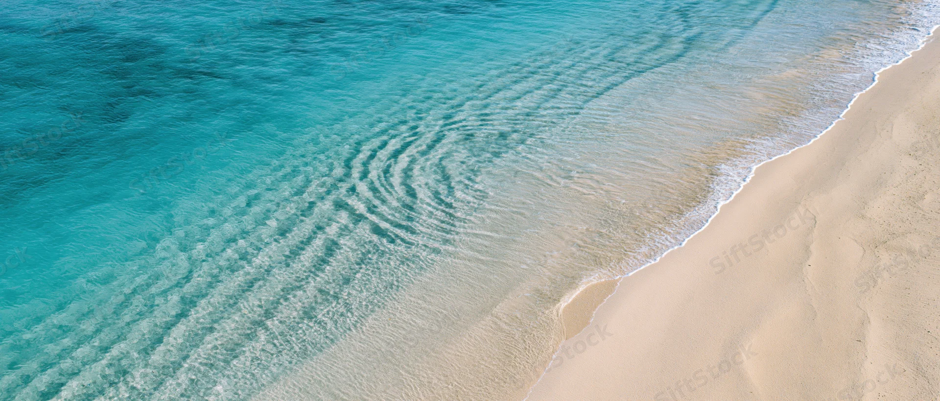 Aerial view of turquoise ocean waves meeting sandy beach shoreline