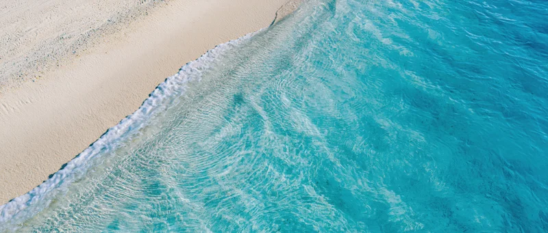 Aerial view of turquoise ocean waves meeting white sandy beach at tropical shoreline