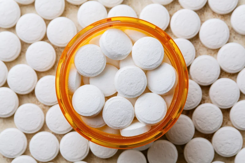 Overhead close-up of white tablets in an open orange prescription bottle on a bed of pills