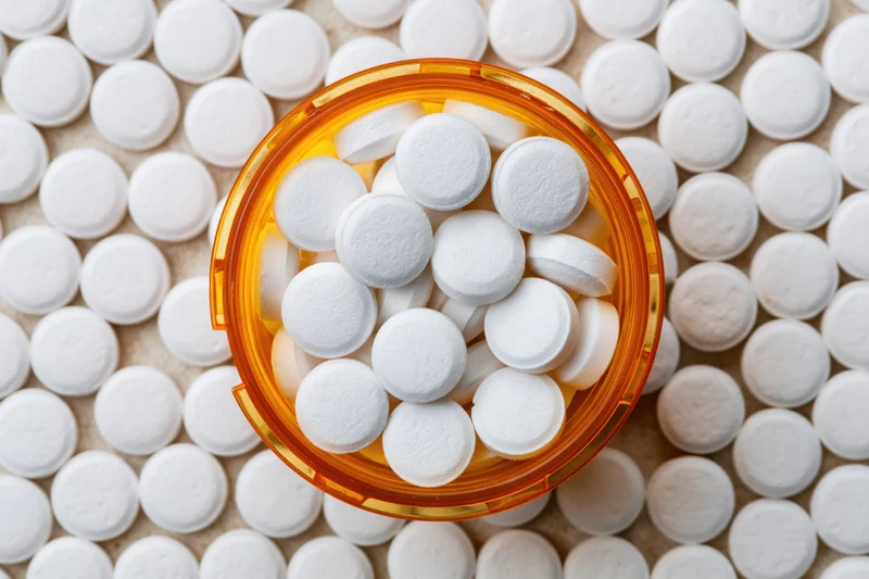 Overhead close-up of white tablets in an open orange prescription bottle on a bed of pills