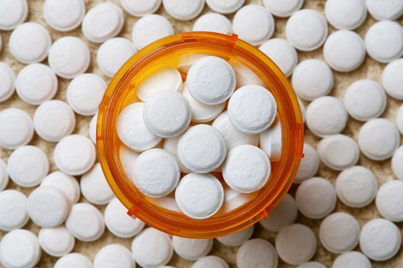 Overhead close-up of white pills in an open orange prescription bottle on a textured surface