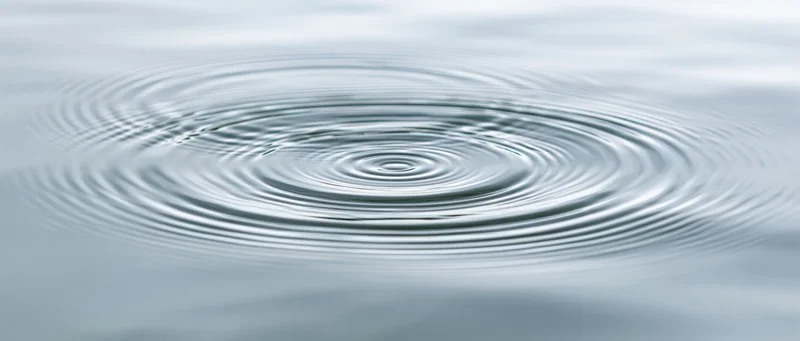Overhead closeup of calm shallow water surface with concentric ripples spreading from center
