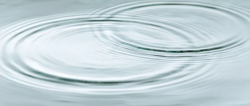 Overhead closeup of calm shallow water surface with two overlapping ripples
