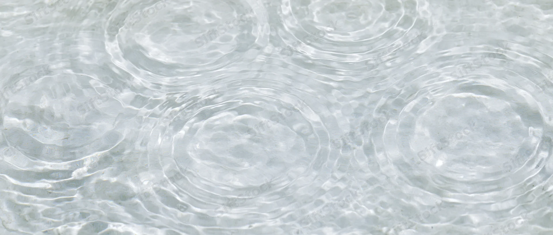 Overhead closeup of shallow clear water surface with circular ripples and light reflections