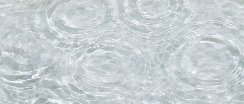 Overhead closeup of shallow clear water surface with circular ripples and light reflections