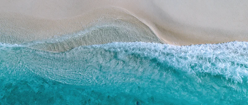Overhead view of turquoise waves breaking on a pale sandy shoreline