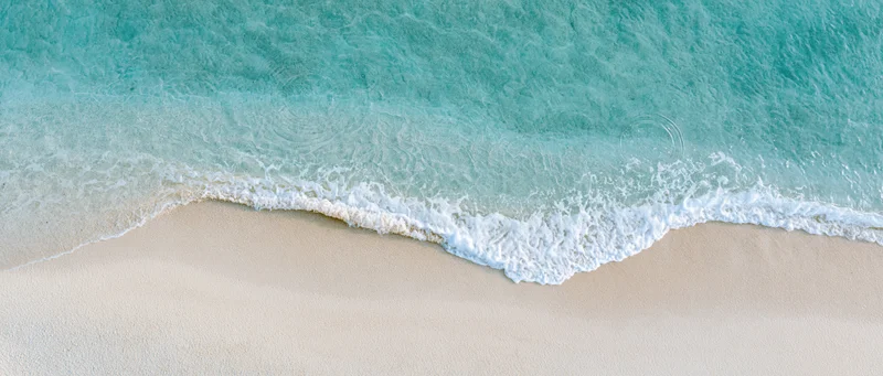 Overhead view of turquoise waves meeting white sand at shallow shoreline