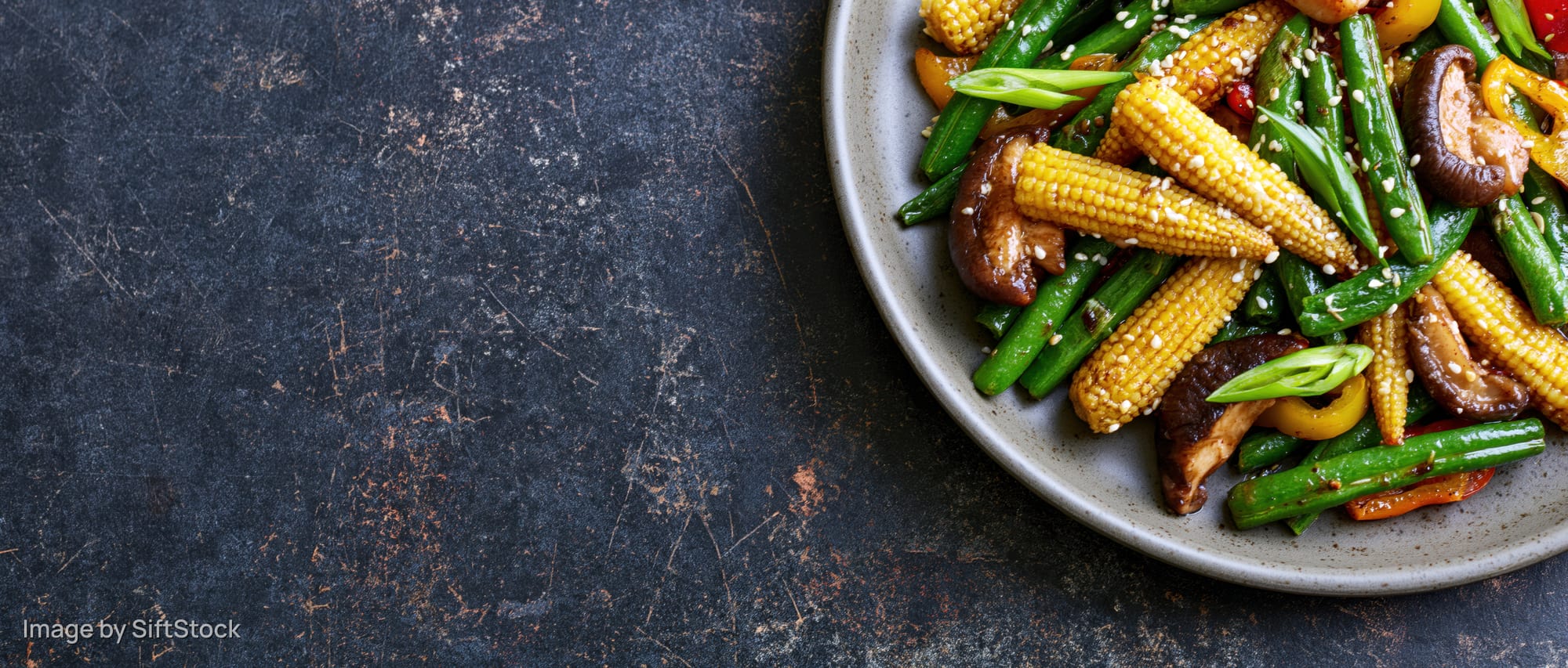 Stir-fried vegetables and mushrooms on a gray plate with sesame seeds on a dark textured surface