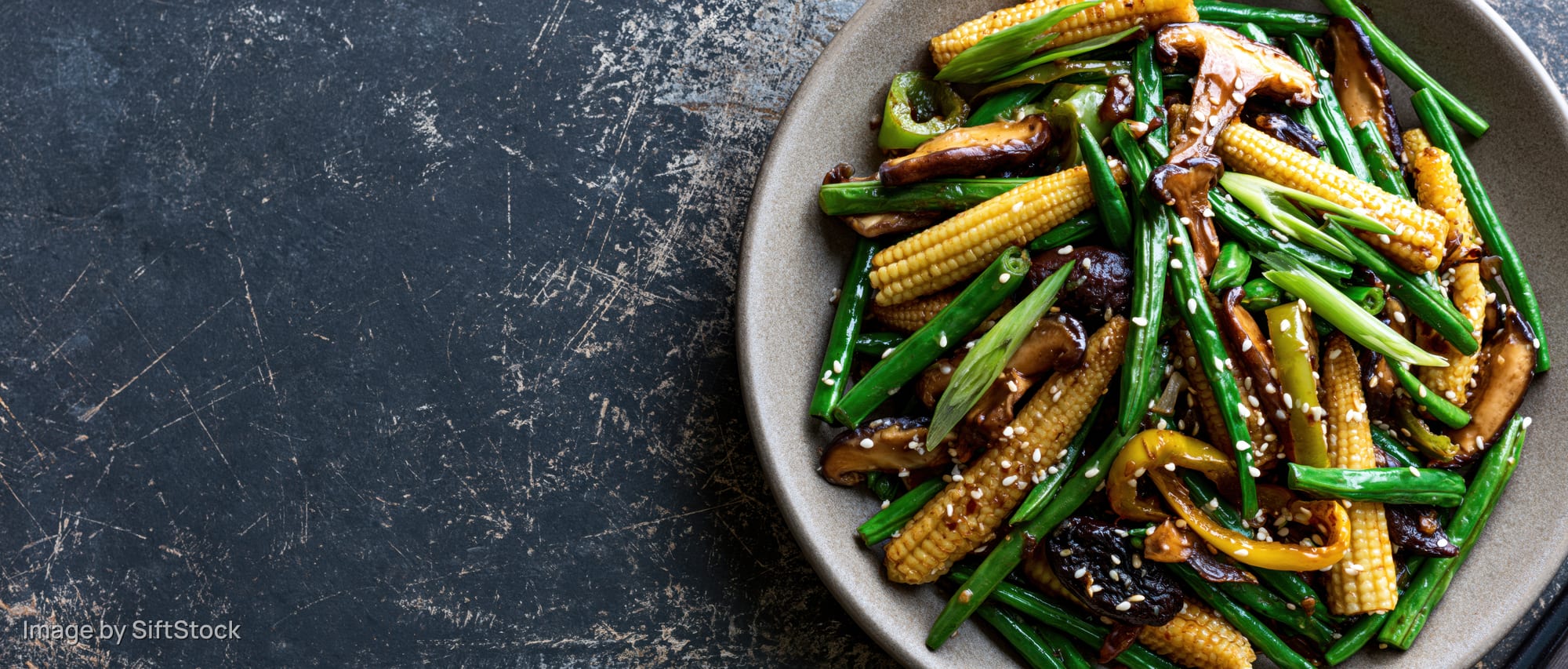 Stir-fried vegetables and mushrooms with baby corn and sesame seeds on a plate over dark textured surface