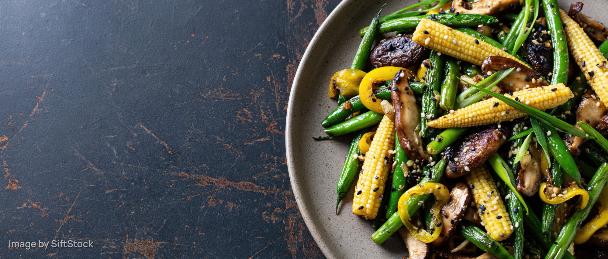 Stir-fried vegetables and mushrooms with corn and peppers on a plate on a dark textured surface