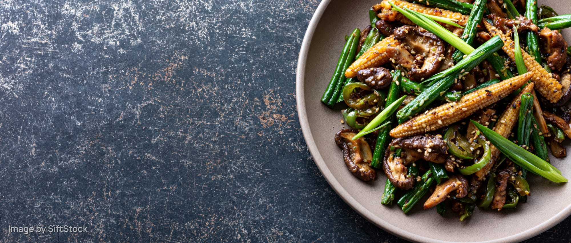 Stir-fried vegetables and mushrooms with baby corn and green onions on a plate over dark textured surface