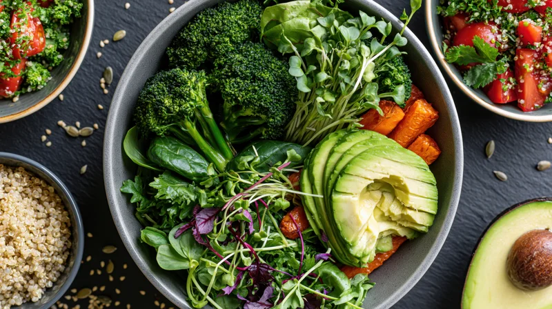 Overhead view of a grey ceramic bowl filled with sliced avocado, broccoli, microgreens, carrots, and spinach, surrounded by small bowls of quinoa and tomato salad on a dark surface
