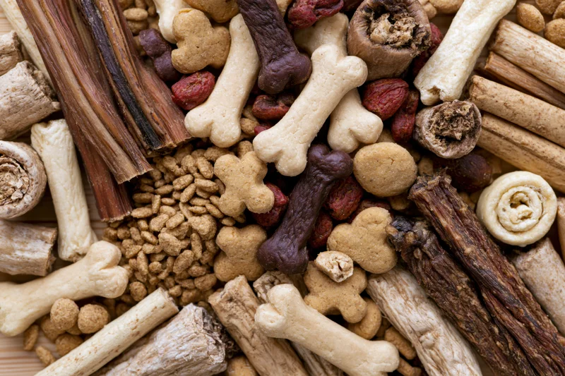 Overhead flat lay of assorted dog treats and pet snacks densely arranged on a wooden surface
