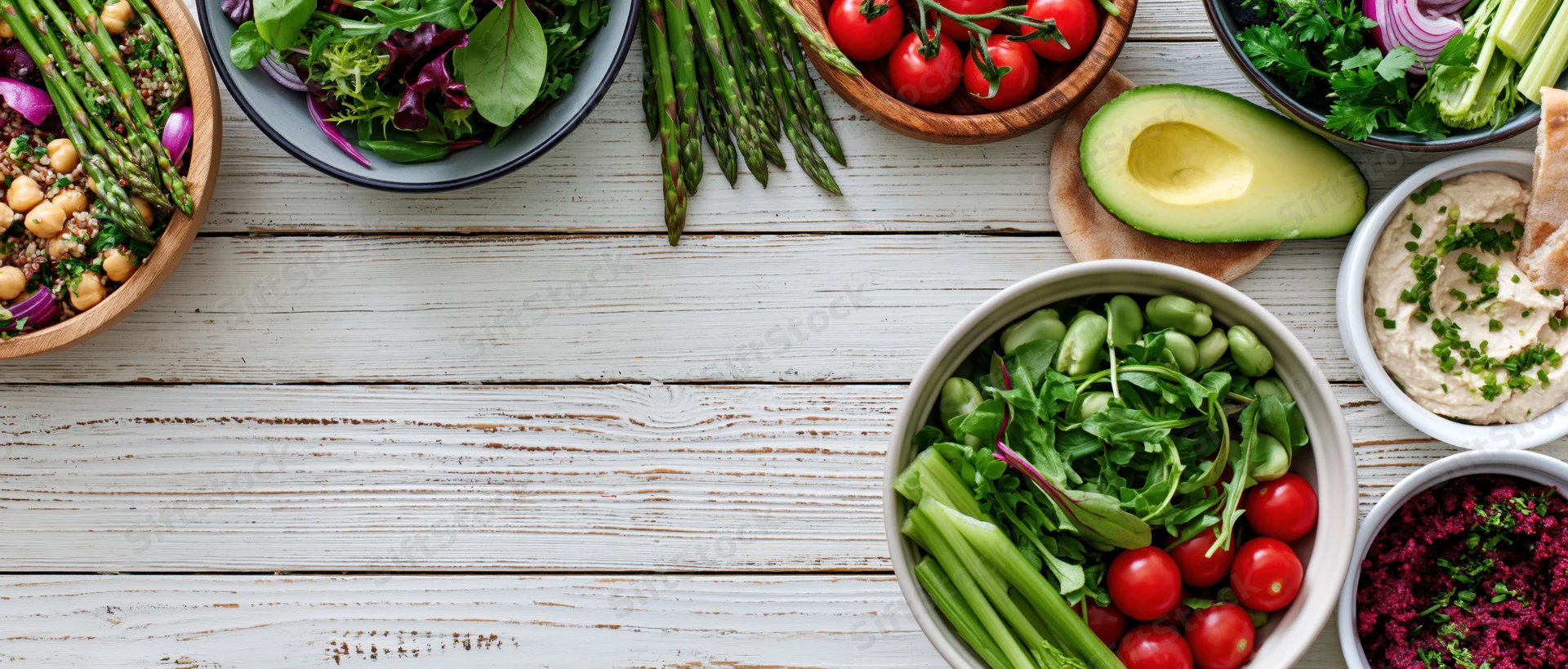 Overhead flat lay of assorted healthy vegetarian dishes and snacks on a white wooden table with copyspace