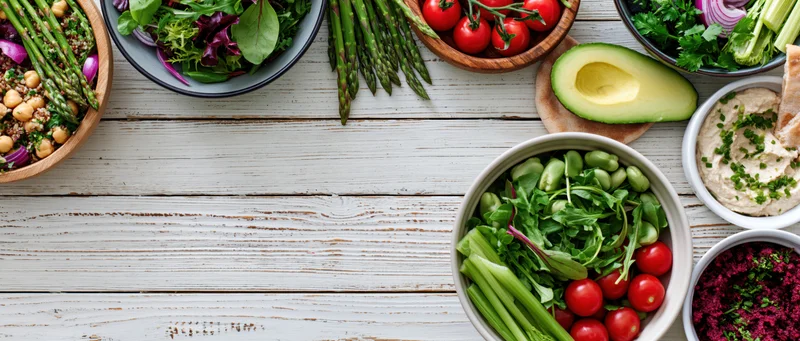 Overhead flat lay of assorted healthy vegetarian dishes and snacks on a white wooden table with copyspace