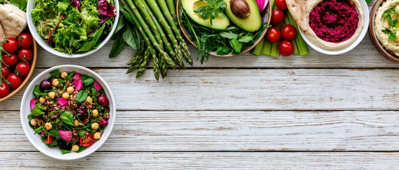 Overhead flat lay of assorted healthy vegetarian dishes and salads on a white wooden table with copyspace
