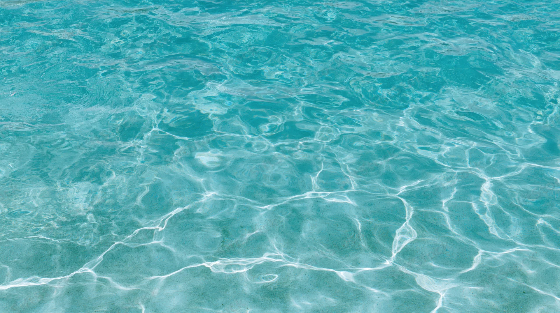 Overhead view of gently rippling turquoise swimming pool water surface with light reflections