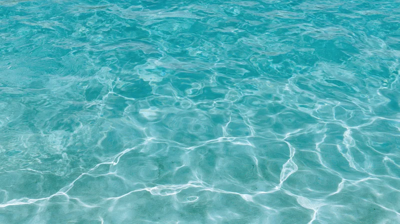 Overhead view of gently rippling turquoise swimming pool water surface with light reflections