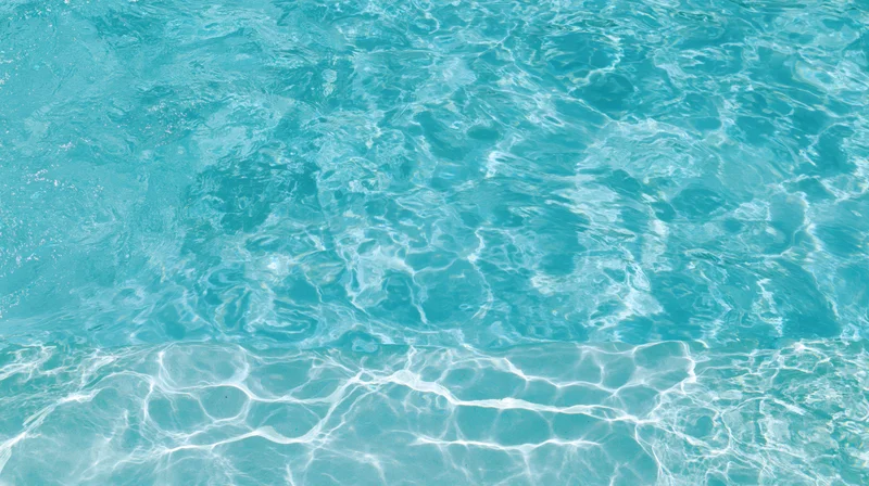 Overhead view of gently rippling swimming pool water surface with sunlight reflections