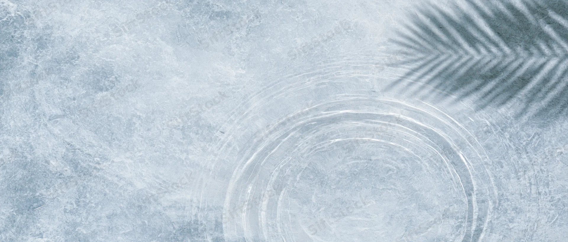 Shallow clear water with circular ripples and palm frond shadow on textured grey-blue surface