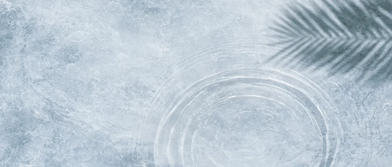 Shallow clear water with circular ripples and palm frond shadow on textured grey-blue surface