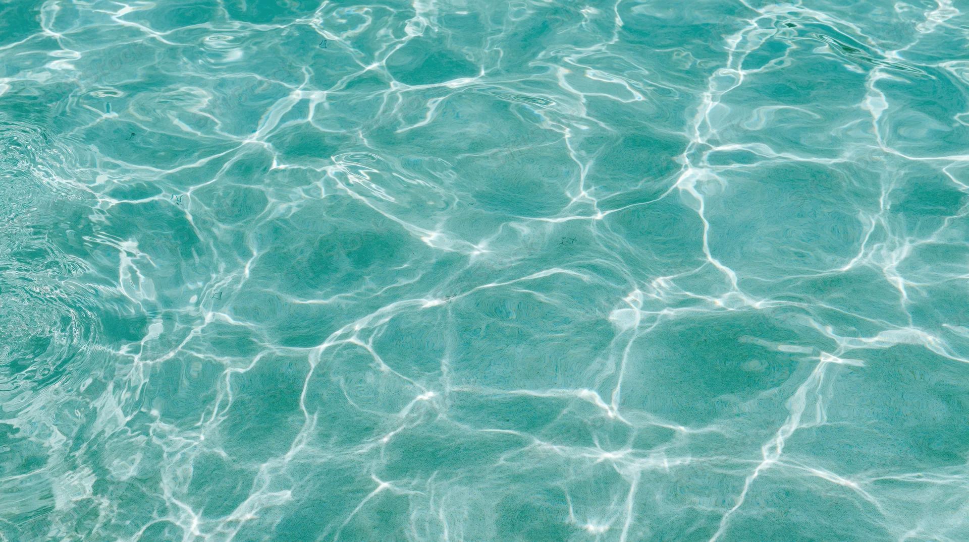 Overhead view of rippling turquoise swimming pool water surface with light reflections and tile pattern visible beneath