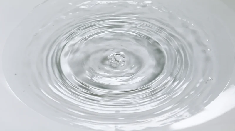 Overhead view of rippling water surface with concentric circles and central droplet impact in a white bowl