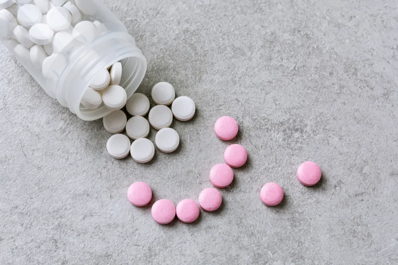 Spilled white and pink tablets from an overturned plastic pill bottle on a gray textured surface