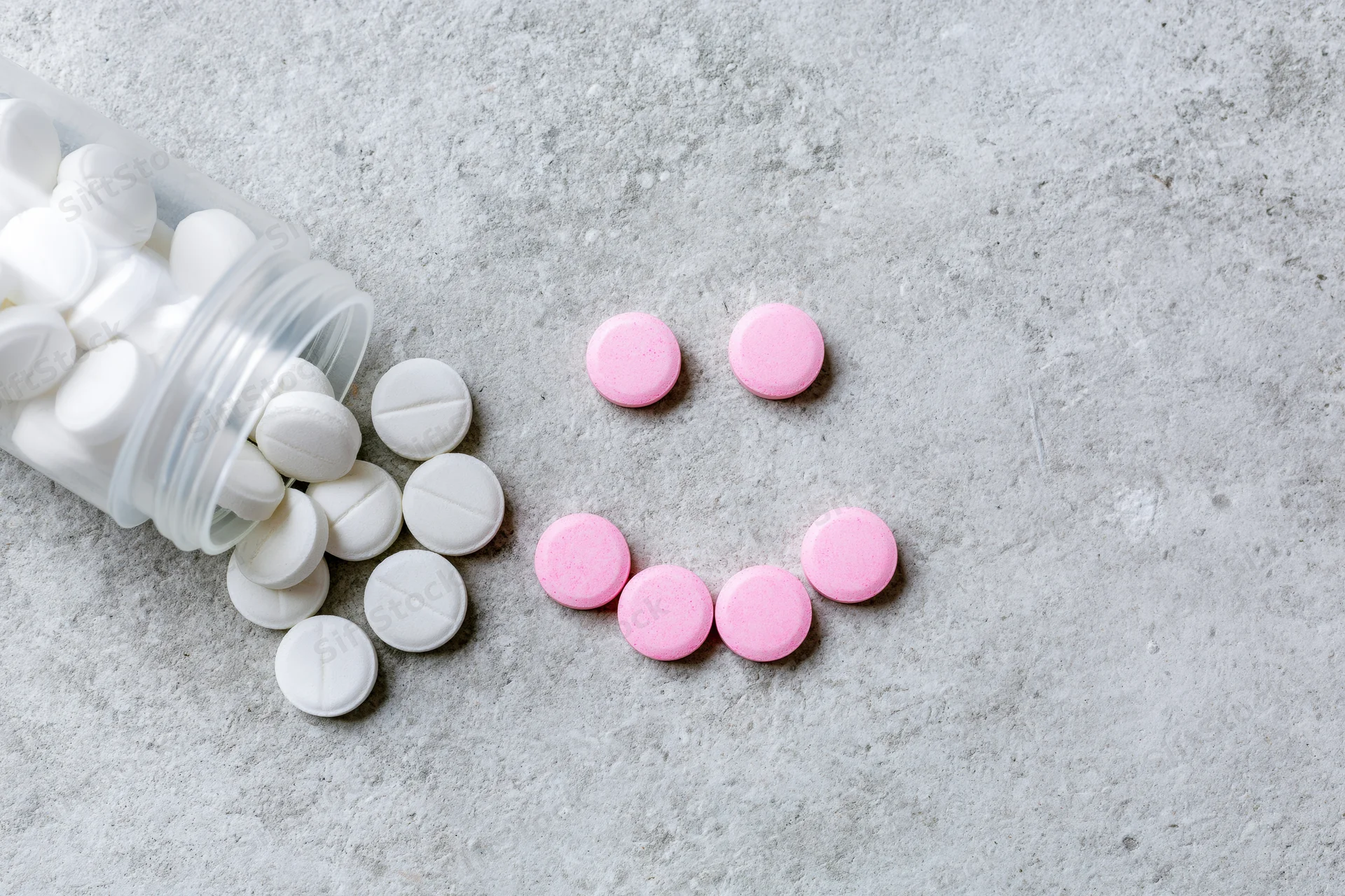Overturned plastic pill bottle with white and pink tablets spilled on concrete surface