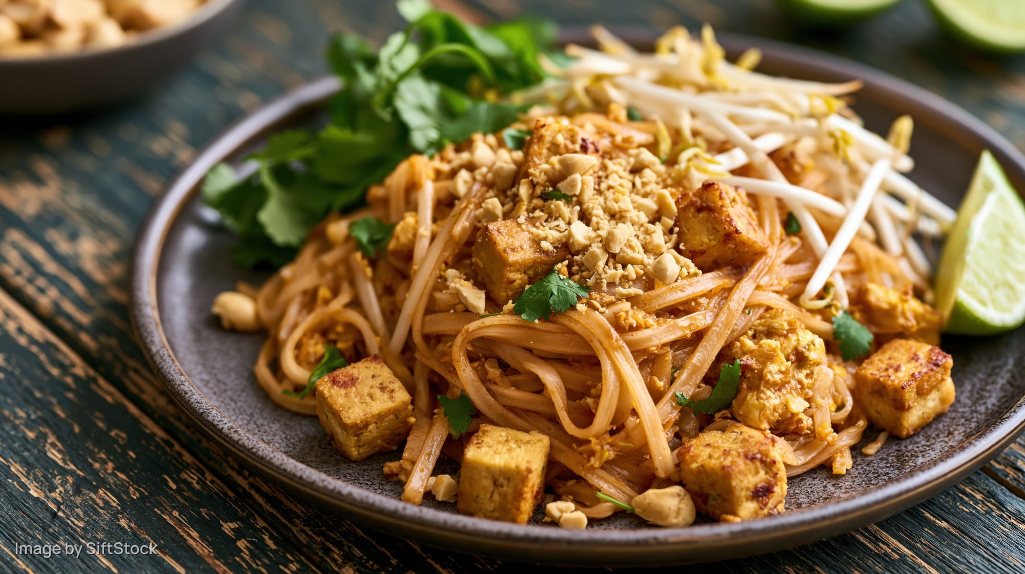 Pad thai noodles with cubed tofu and crushed peanuts on a dark plate on a wooden table