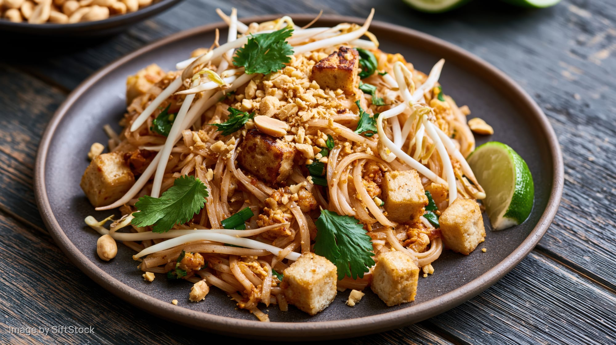 Pad thai noodles with tofu and peanuts on a dark plate on a wooden table