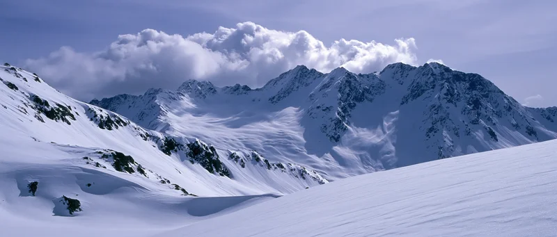 Snow-covered alpine mountains under cloudy sky with glacier and rocky ridges