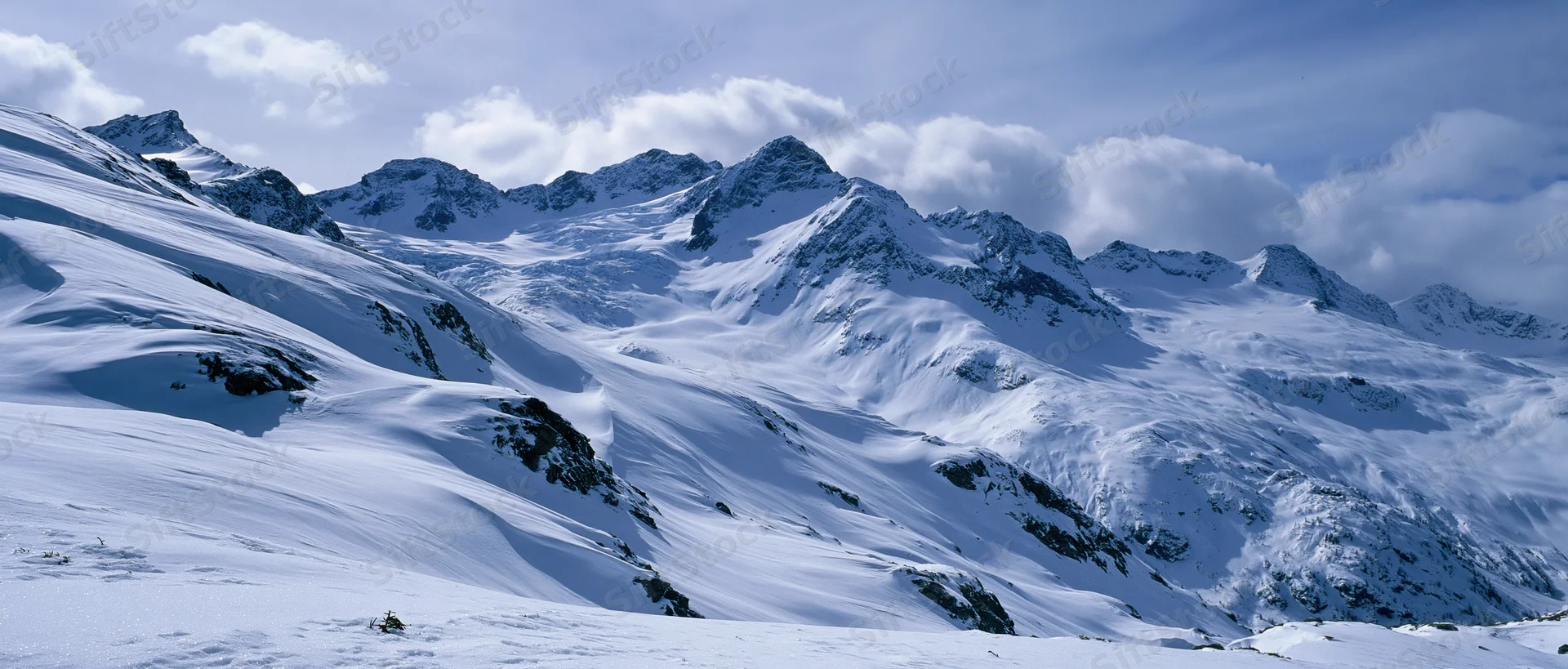 Snow-covered alpine mountains under cloudy sky in panoramic view