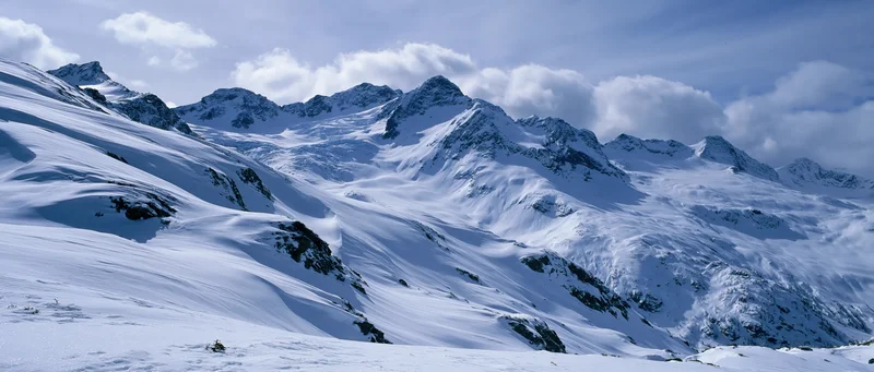 Snow-covered alpine mountains under cloudy sky in panoramic view