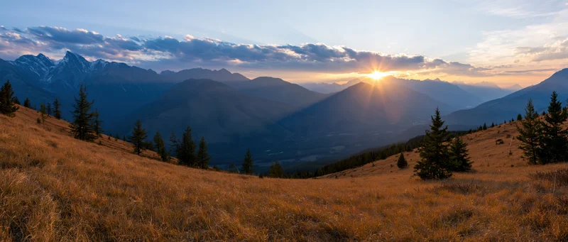 Panoramic alpine landscape at golden hour sunset with layered mountains and grassy meadow in foreground