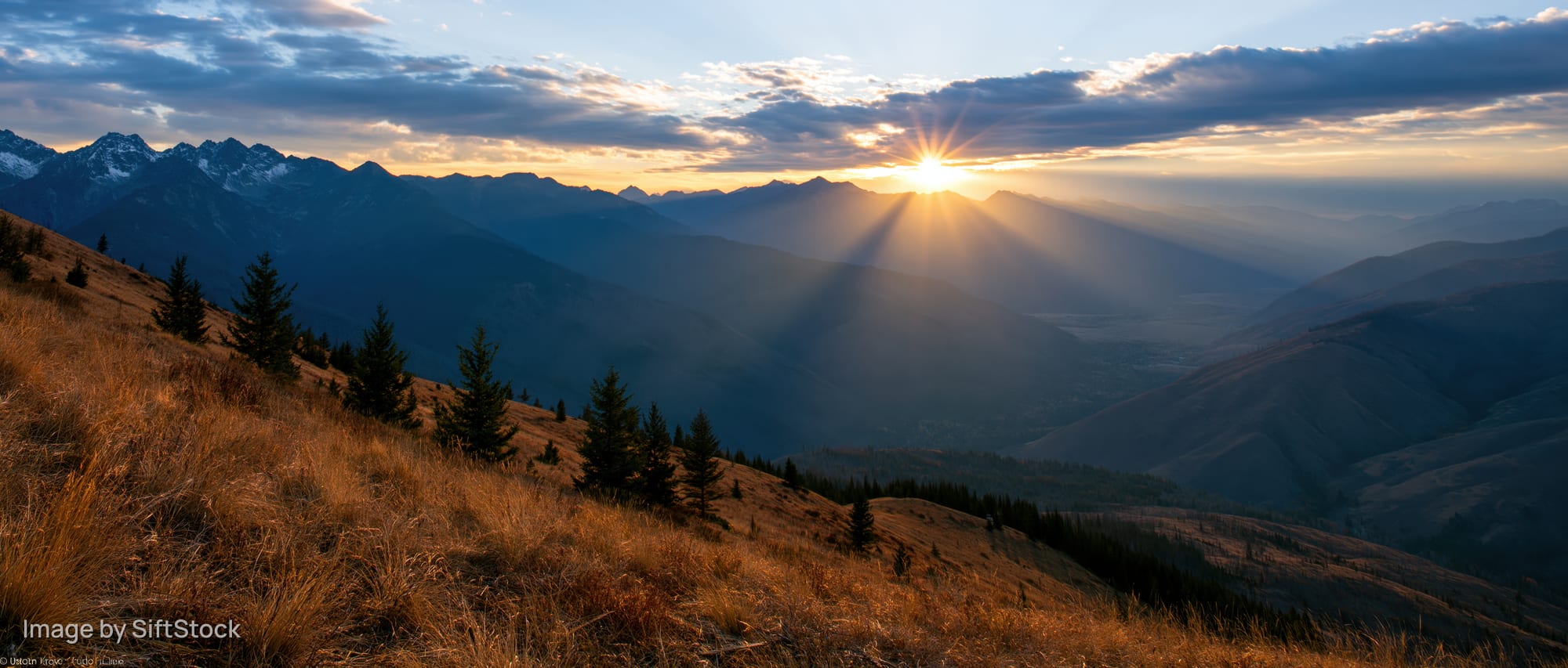 Panoramic alpine landscape at golden hour sunset with sun rays over mountain valley and grassy ridge