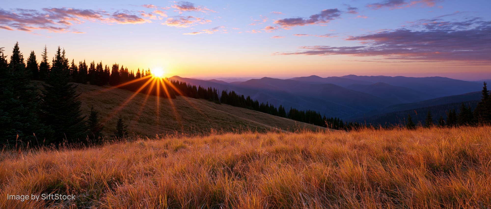 Golden sunset over mountain meadow with sunburst and distant hills