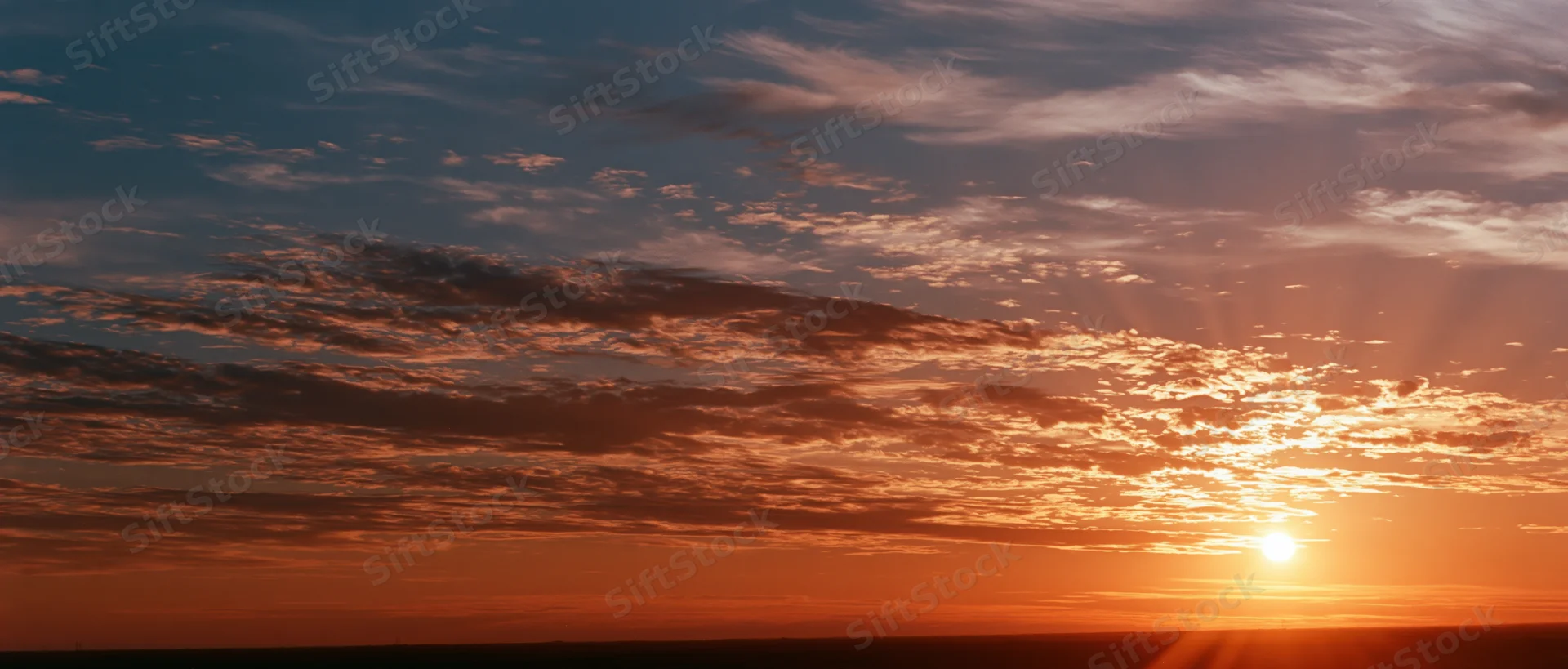 Sunrise over a wide sky with scattered clouds and warm light above the horizon
