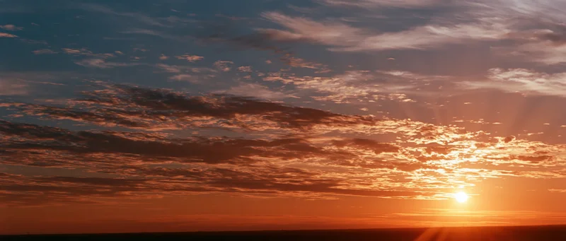 Sunrise over a wide sky with scattered clouds and warm light above the horizon