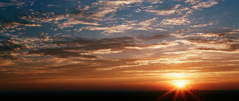 Sunrise over the horizon with scattered clouds and sunrays in a panoramic sky view