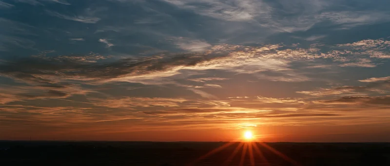 Sunrise over a wide horizon with sun rays and scattered clouds in the sky