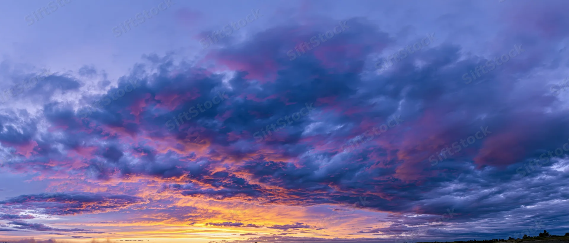 Panoramic view of a dramatic sunset sky filled with cumulus clouds over a rural horizon